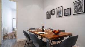 Un coin repas avec une table en bois dressée pour quatre personnes, des chaises à revêtement gris et des photographies encadrées de noir accrochées au mur.
