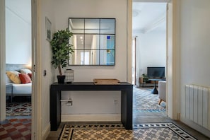 Un couloir avec une console noire, une plante en pot, un miroir et un sol à motifs.