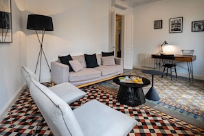 A living room with a sofa, armchairs, a coffee table, a floor lamp, and a dining area with a table and chairs.