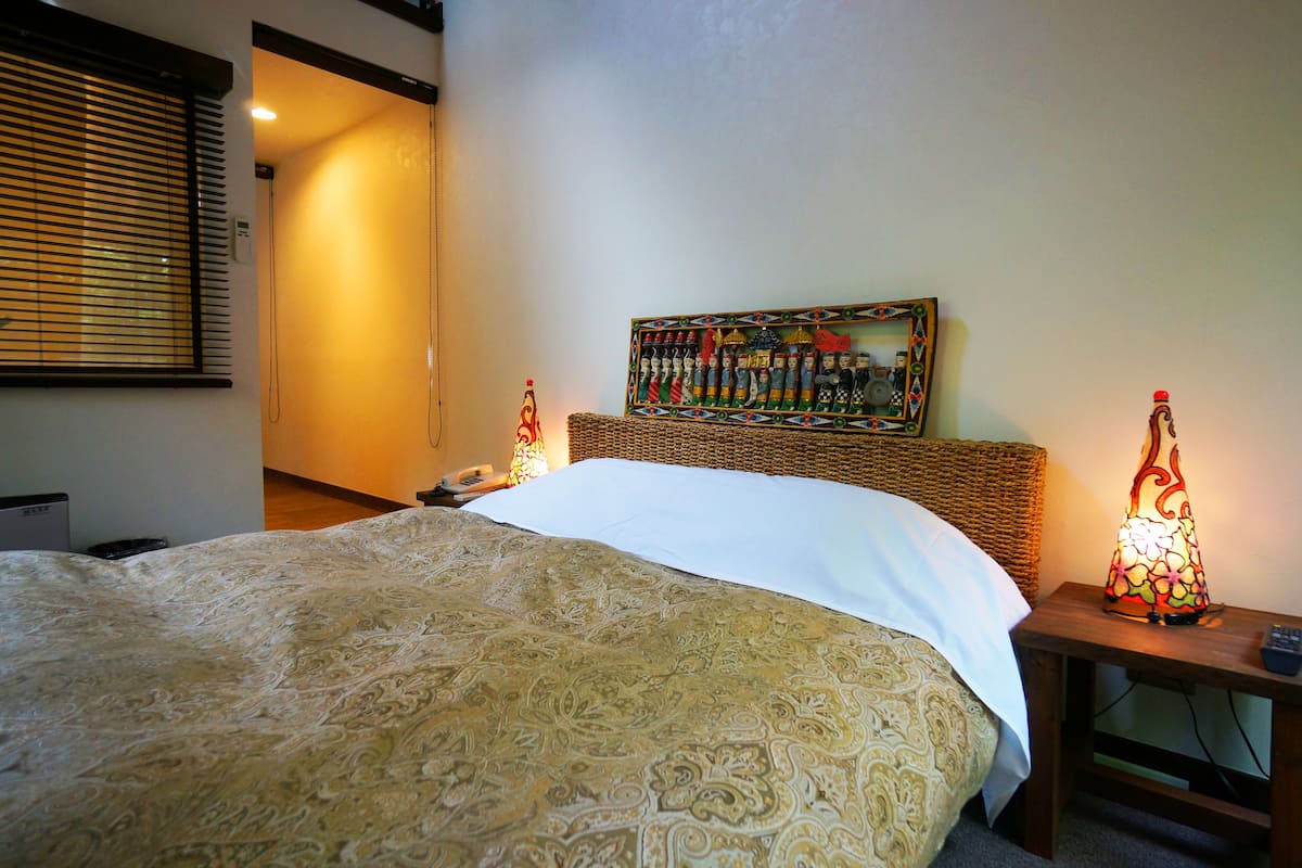 A neatly made bed with a patterned bedspread, a wicker headboard, and two wall-mounted lamps.
