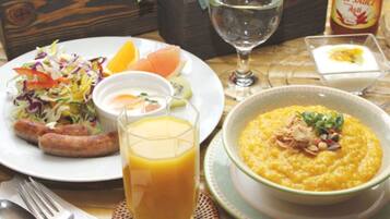 A meal with sausages, salad, and a bowl of porridge, along with a glass of orange juice and a bottle of chili sauce.