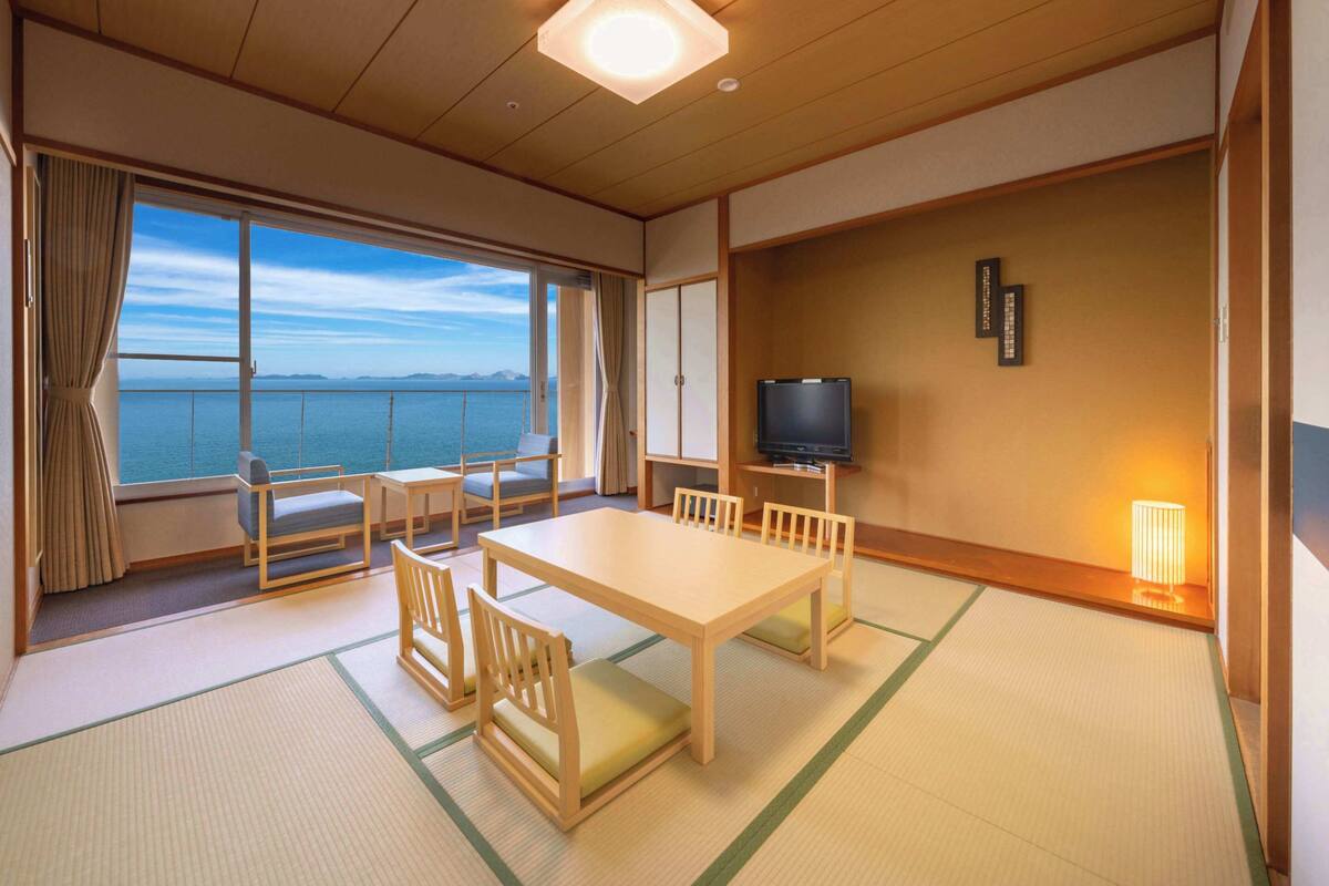 Ein Zimmer mit Holztisch und -stühlen, einem Fernseher und Meerblick.
