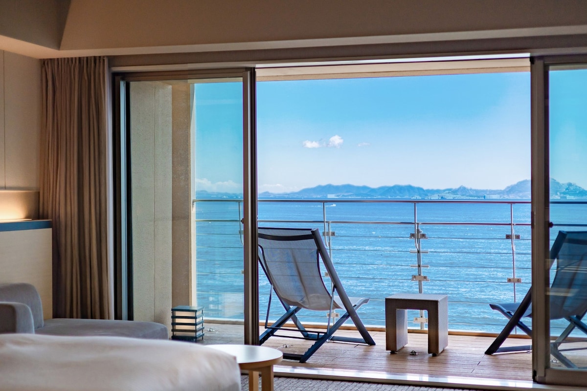 A hotel room with a large sliding glass door leading to a balcony with two chairs and a small table.
