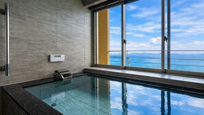 A modern indoor swimming pool with a clear view of the ocean through large windows.