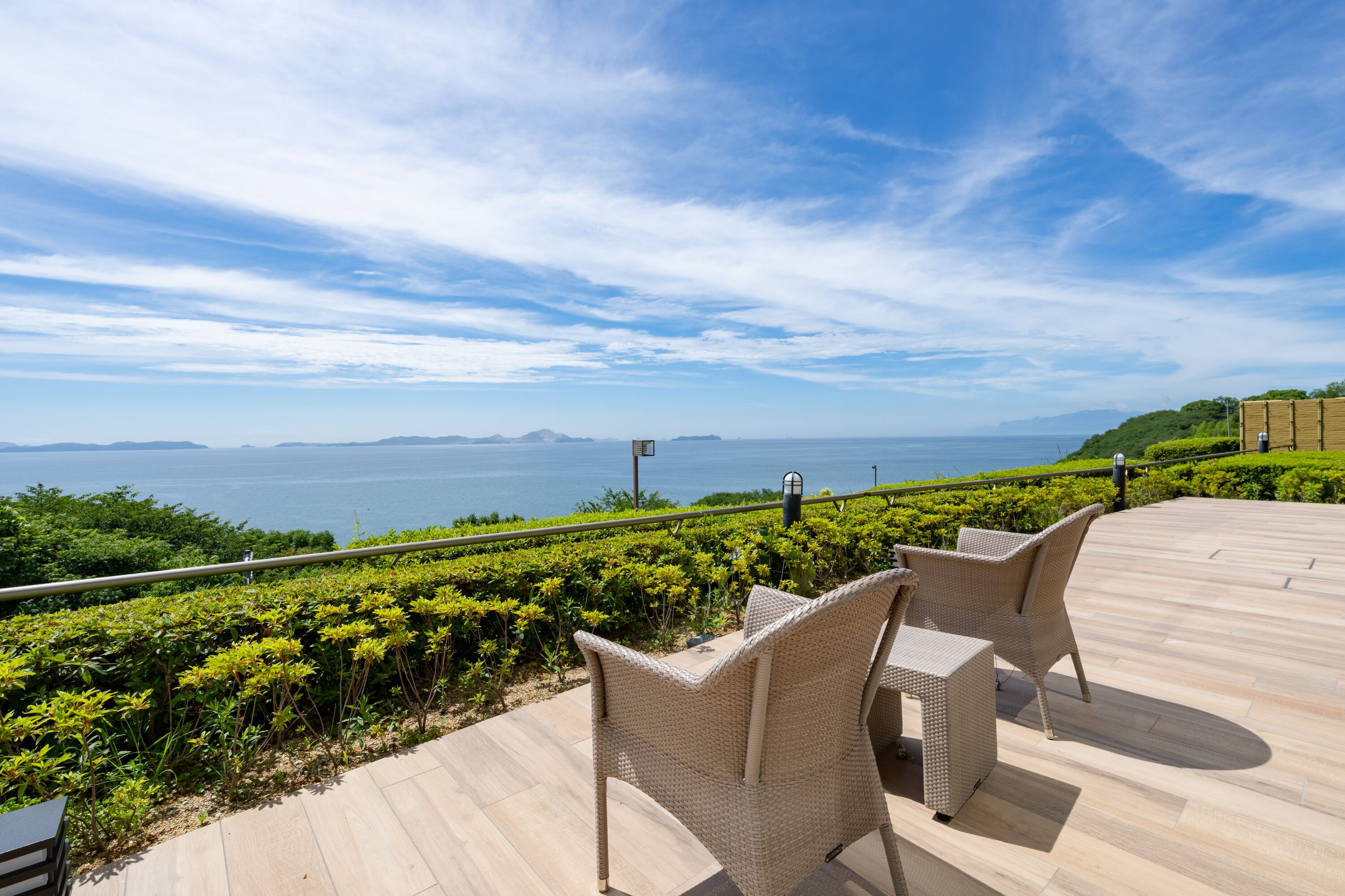 Una terraza con mobiliario de mimbre que ofrece vistas panorámicas del mar y unas islas a lo lejos.