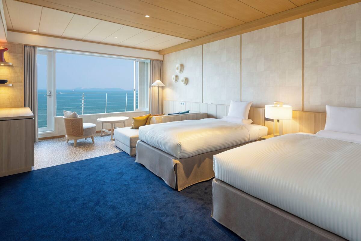 Ein Hotelzimmer mit zwei Betten, einer Sitzecke und Meerblick sowie einem kleinen Tisch.