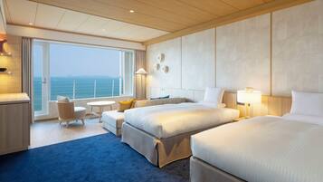 Habitación de hotel con dos camas, una zona de estar y vista al mar, y una pequeña mesa.