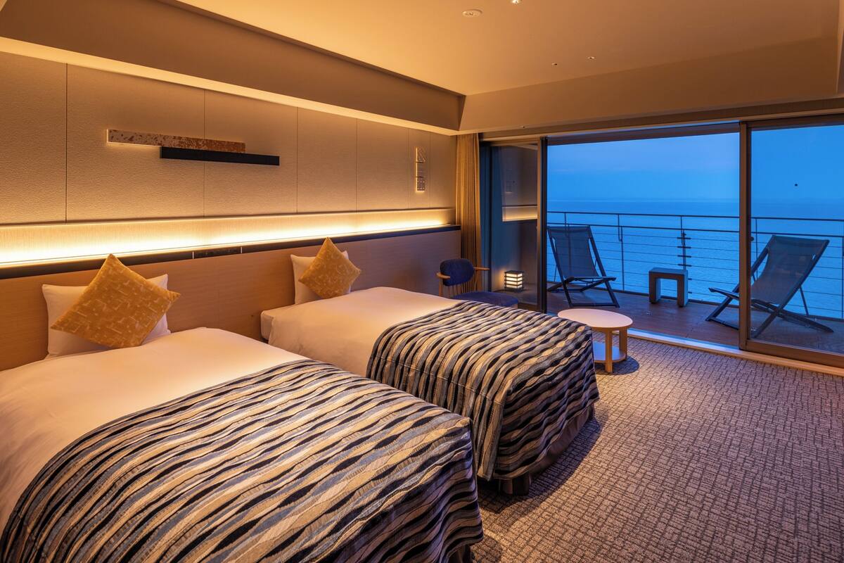 Ein Hotelzimmer mit zwei Betten, einem kleinen Tisch und einem Balkon mit Meerblick.