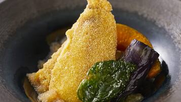 A dish with breaded food, possibly chicken, accompanied by greens and a slice of orange.