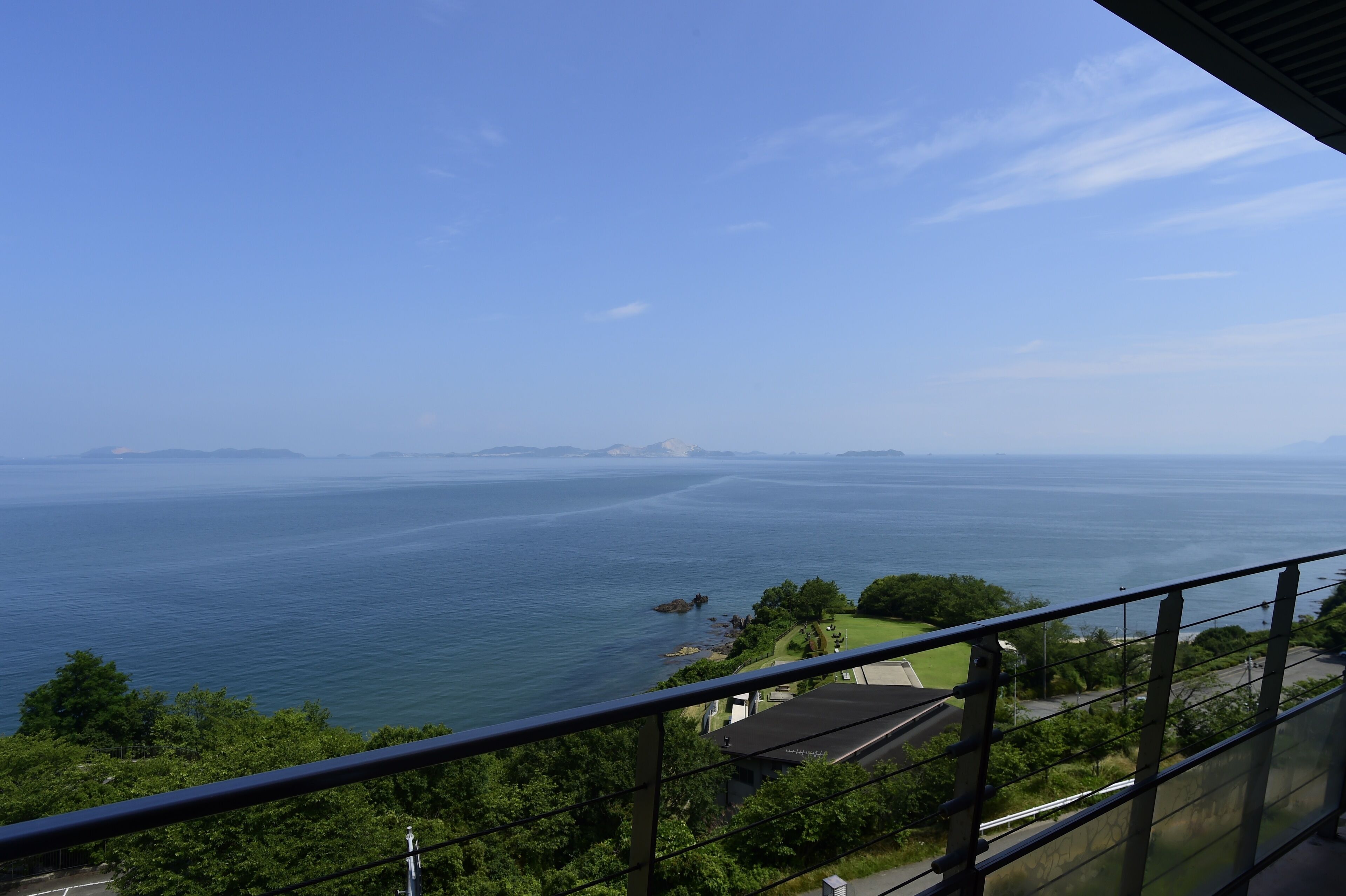 Une vue sur la côte, prise depuis un balcon doté d’une balustrade, donnant sur une mer calme et une terre lointaine.