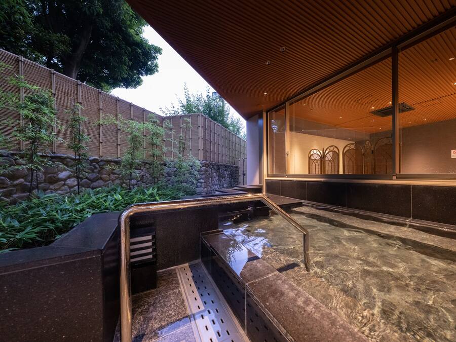 A modern spa area with a stone wall, bamboo plants, and a clear water feature.