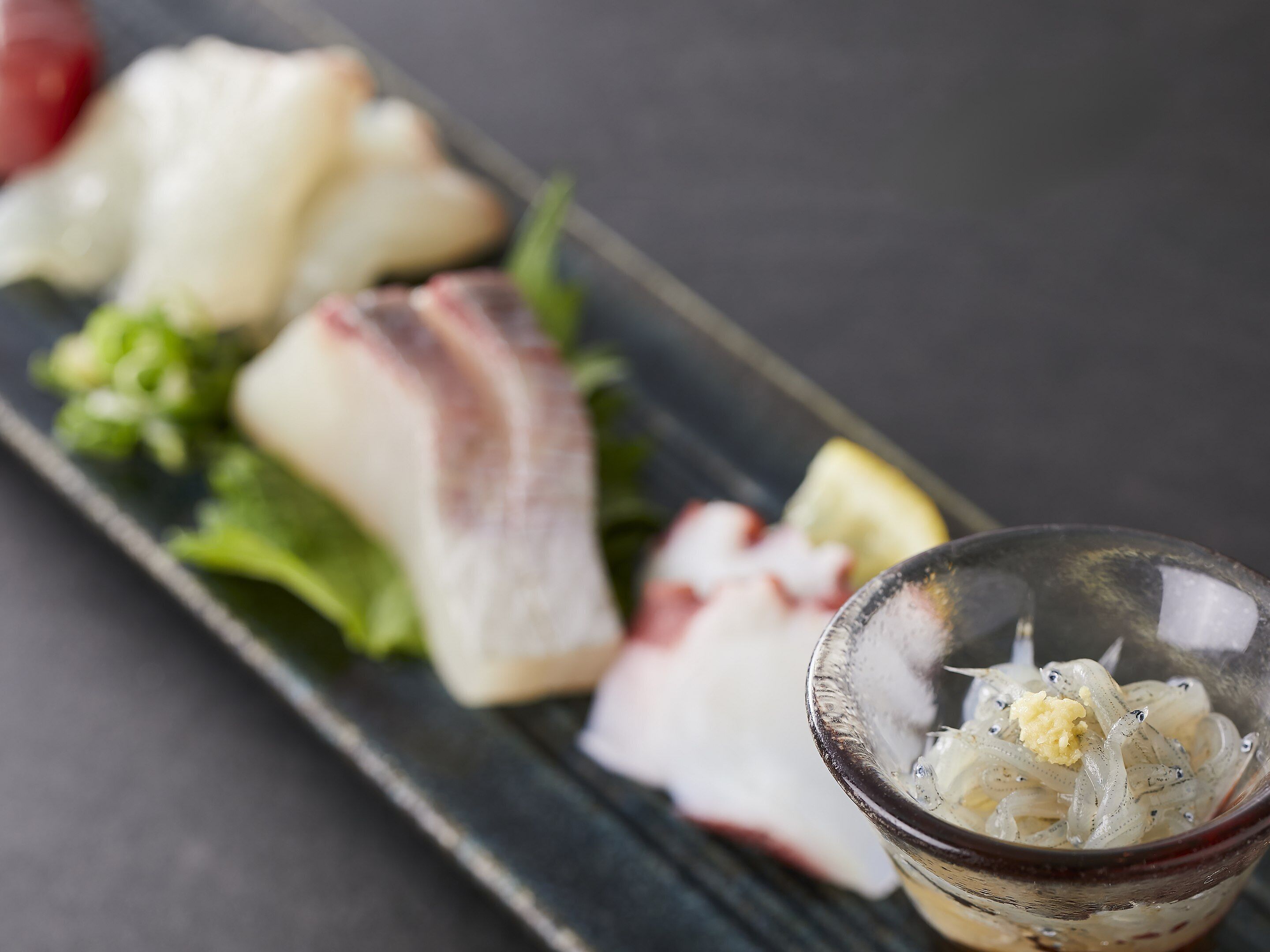 A plate of sashimi with a small bowl of pickled ginger.