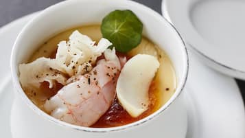 Un bol de soupe aux fruits de mer, garni d’une feuille, posé sur une assiette blanche.