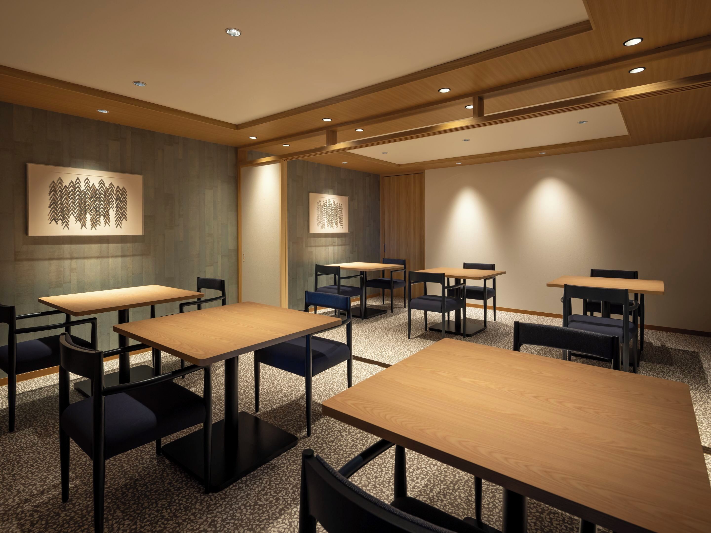 A conference room with multiple tables and chairs, wooden ceiling panels, and recessed lighting.