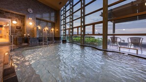 A large indoor pool with a stone floor, surrounded by large windows offering views of the outdoors.