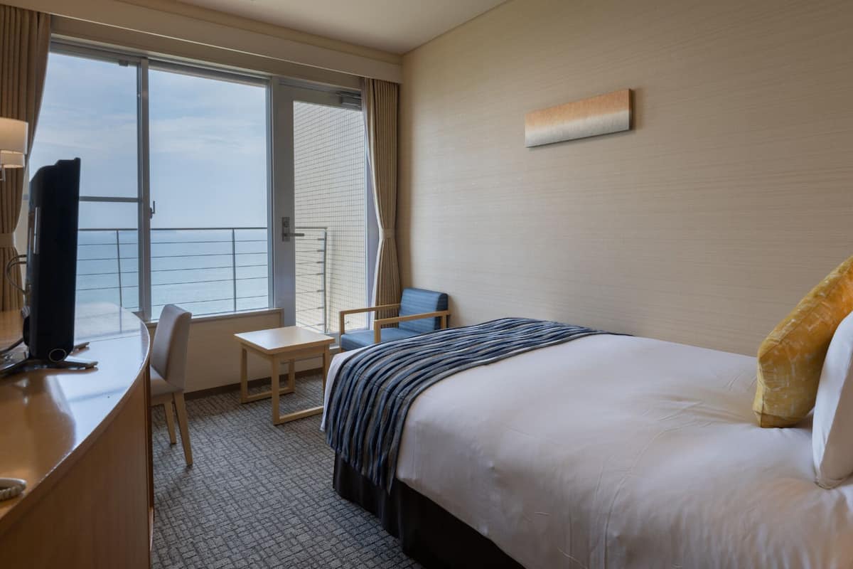 Une chambre d’hôtel équipée d’un lit, d’un bureau, d’une chaise, d’une télévision et d’une fenêtre donnant sur un paysage agréable.