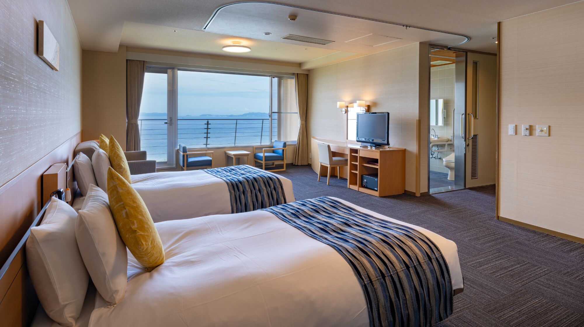Habitación de hotel con dos camas, un escritorio, un televisor y vista al mar.