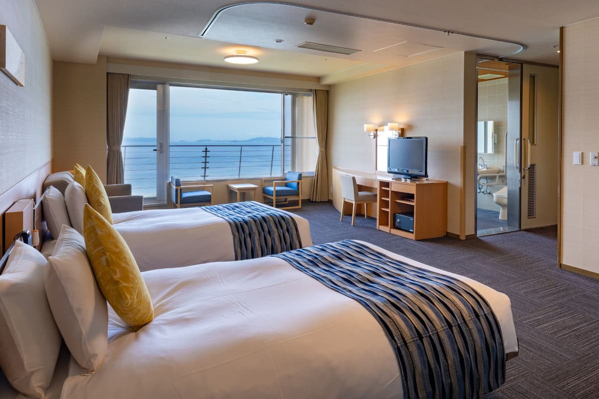 Habitación de hotel con dos camas, un escritorio, un televisor y vista al mar.