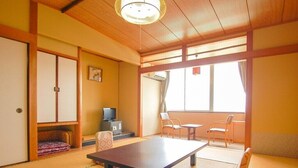 A traditional Japanese room with tatami flooring, a low table, a sofa, and a television.