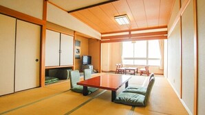 A traditional Japanese room with tatami flooring, a low table, cushions, a television, and sliding doors.