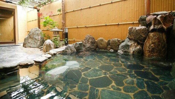 A traditional Japanese onsen with a stone bath surrounded by rocks and bamboo walls.