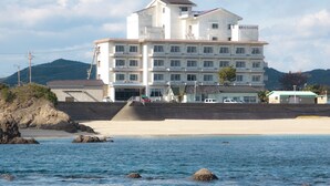A multi-story hotel with a beach view, featuring a staircase leading to the entrance, a parking area, and a sign indicating it is a hotel.