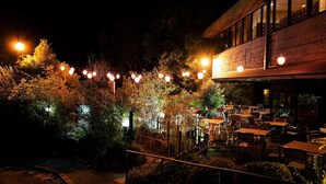 An outdoor dining area with tables and chairs, surrounded by trees and illuminated by string lights. - Sanage Onsen Hotel Kinsenkaku (Toyota)