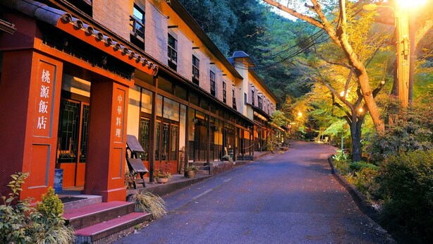 A traditional building with a red facade and multiple windows, surrounded by lush greenery and a paved pathway. - Sanage Onsen Hotel Kinsenkaku (Toyota)