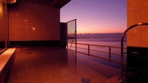 A spacious indoor area with a view of the sea at sunset, featuring a metal railing and a tiled floor. - Ikeuo-no Mifune (Minamichita)