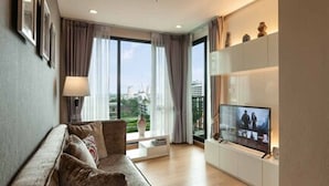 A modern living room with a sofa, a TV, and a view of the outdoors through large windows.