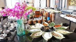 A buffet table with various food items and a vase of pink flowers.