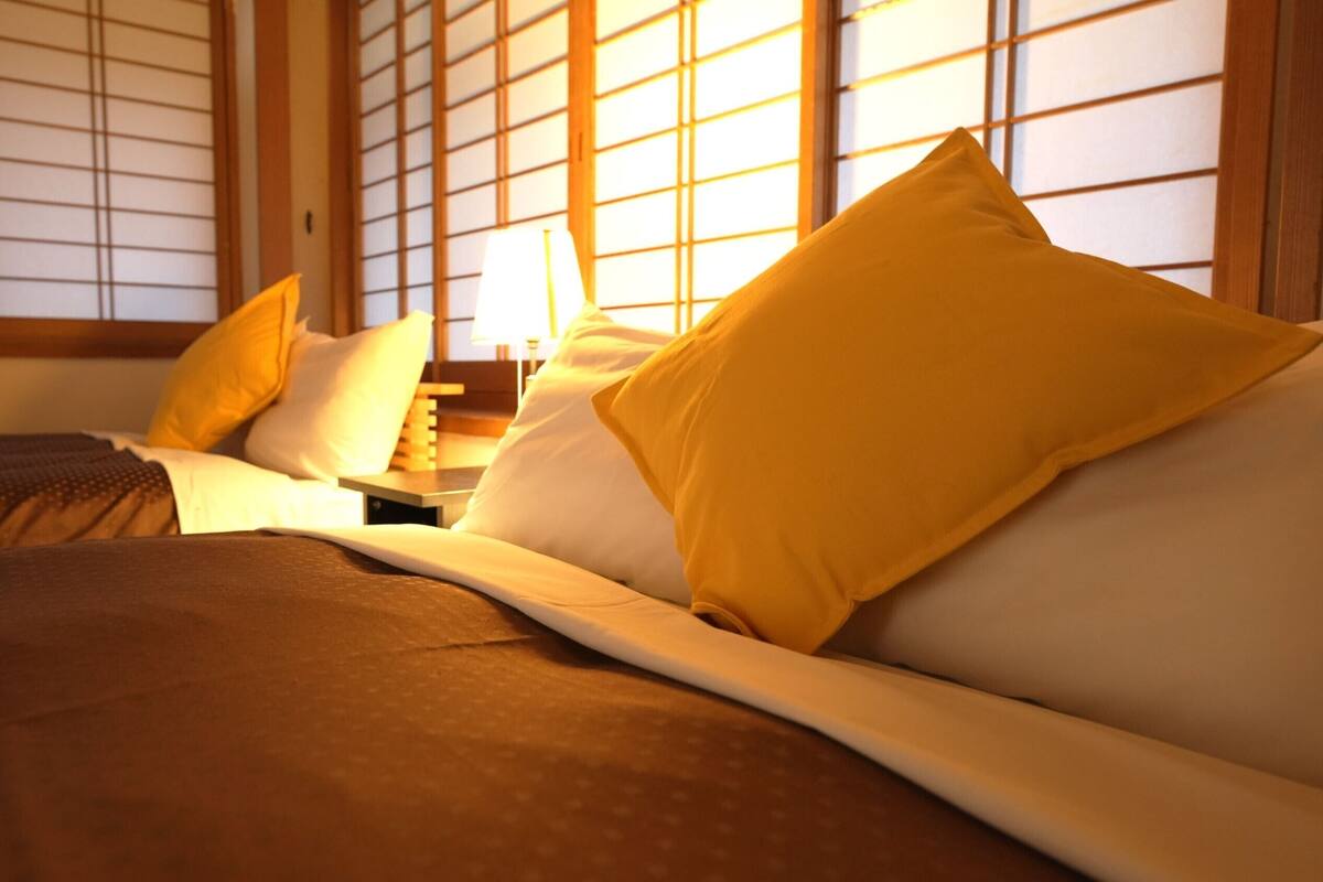 A hotel room with a bed, pillows, a nightstand, and a lamp.