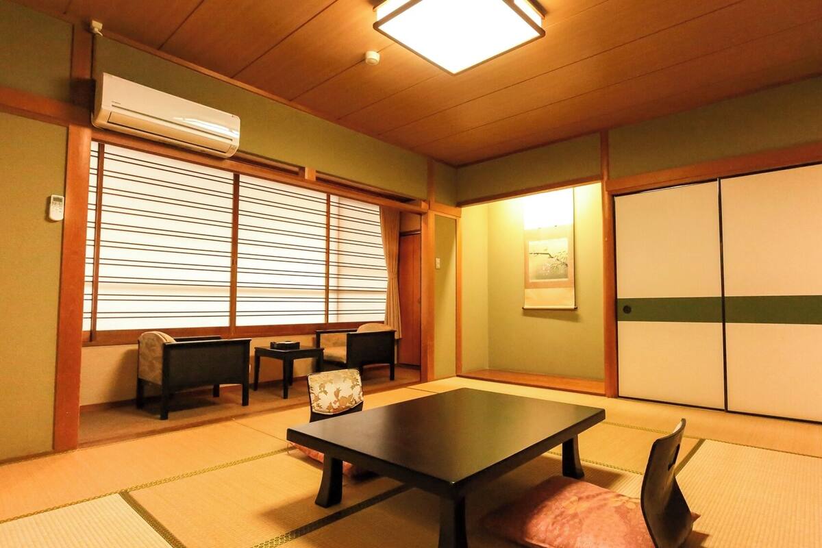 A traditional Japanese room with tatami flooring, a low table, chairs, a sliding door, and an air conditioning unit.