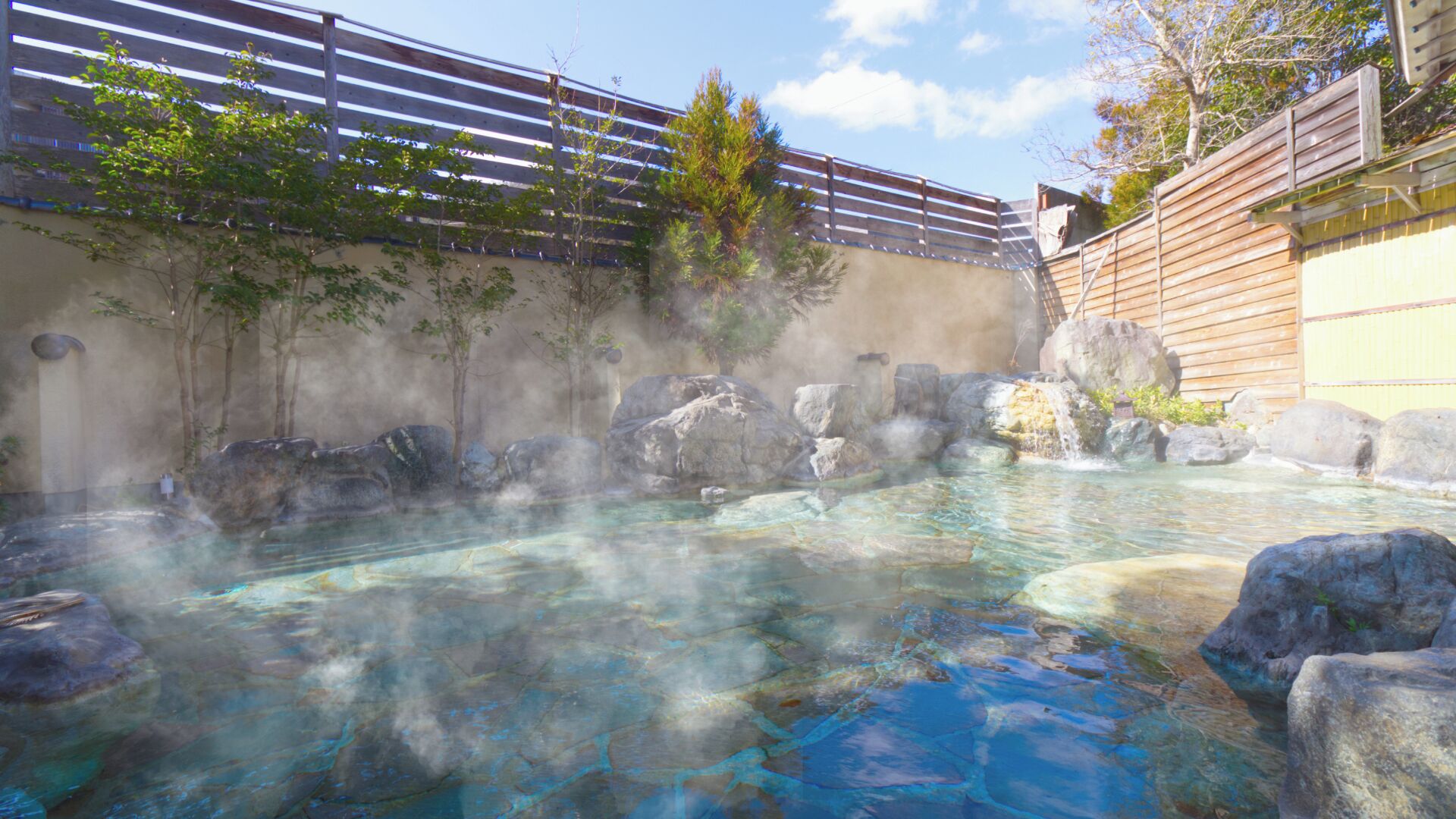 A hot spring area with clear water, rocks, and a wooden fence.