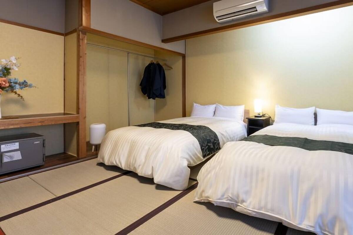 A hotel room with two beds, a wardrobe, a desk, and an air conditioning unit.