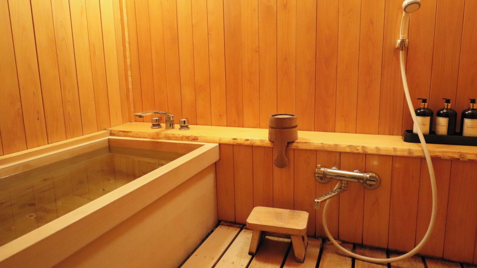 A wooden-paneled bathroom with a bathtub, a shower, and a small stool.