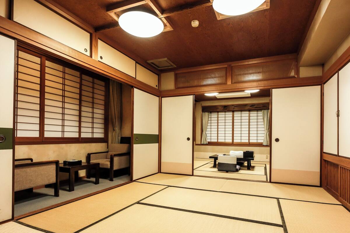 A traditional Japanese room with tatami flooring, sliding doors, and a low ceiling with recessed lighting.