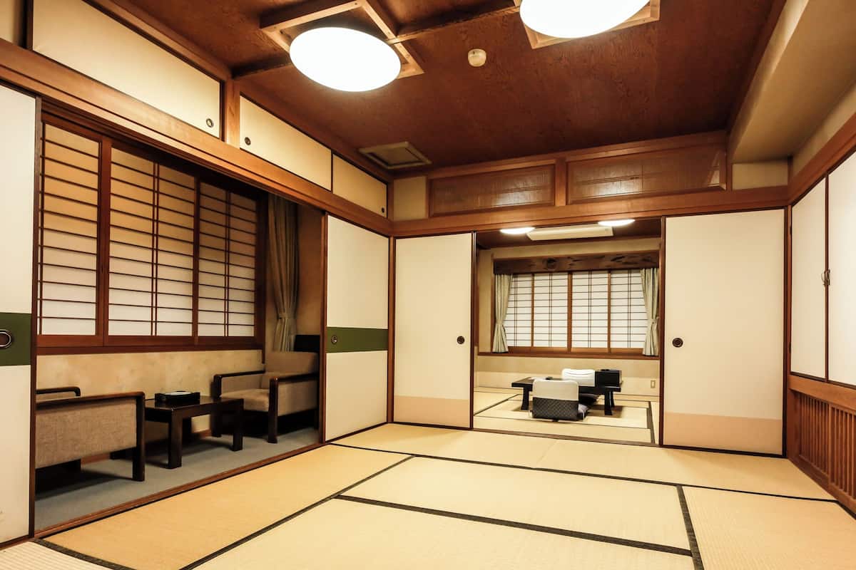 A traditional Japanese room with tatami flooring, sliding doors, and a low ceiling with recessed lighting.