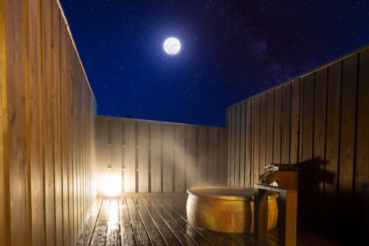 A wooden room with a large round hot tub, a wooden bench, and a wooden wall.