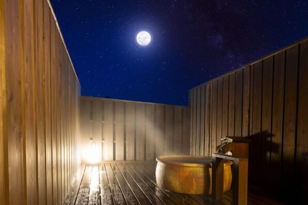 A wooden room with a large round hot tub, a wooden bench, and a wooden wall.