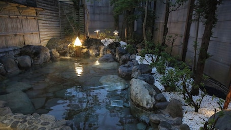 A traditional Japanese garden with a stone pond, rocks, and bamboo plants.