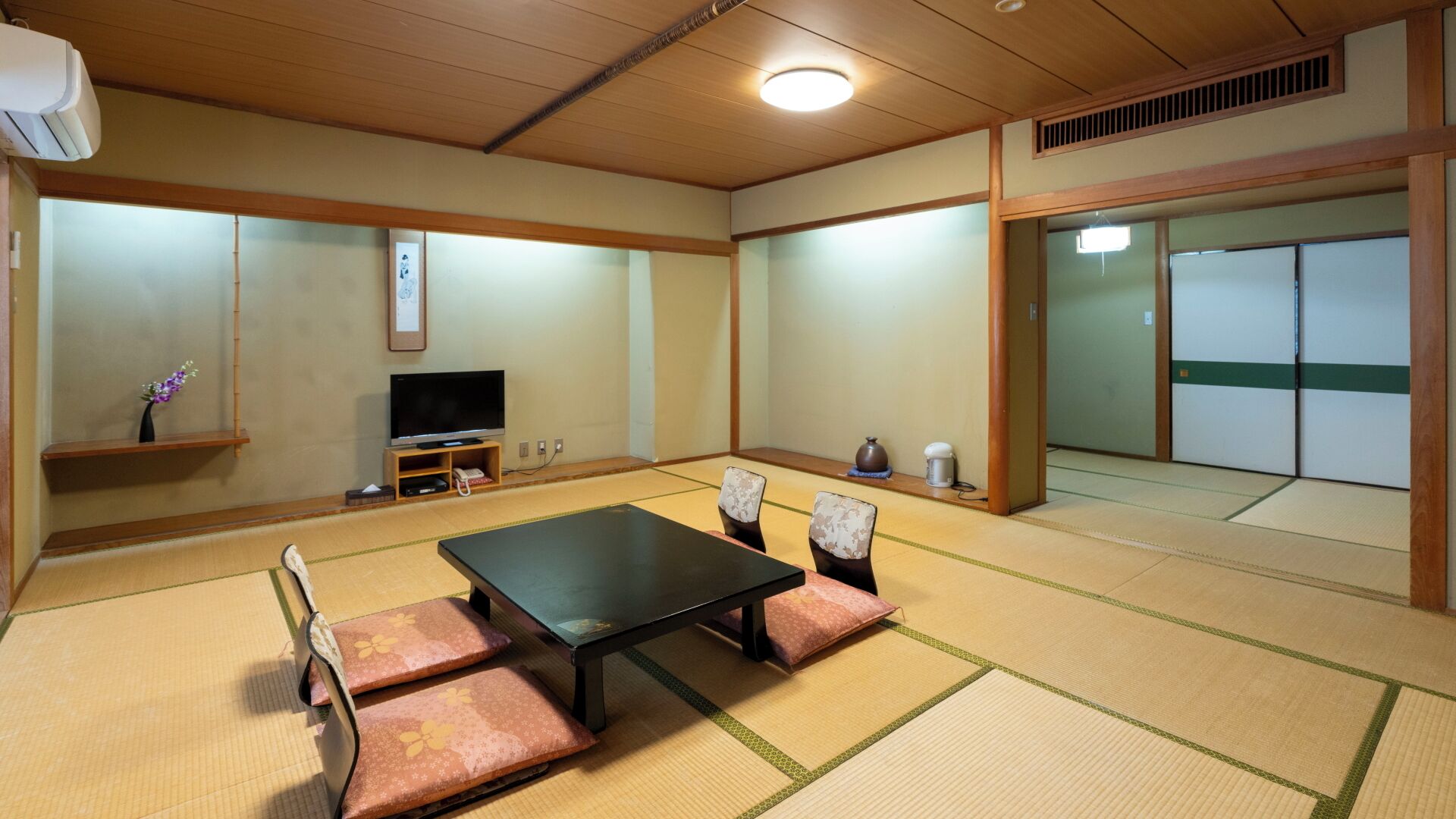 A tatami mat room with a television, cushions, and a traditional Japanese aesthetic.