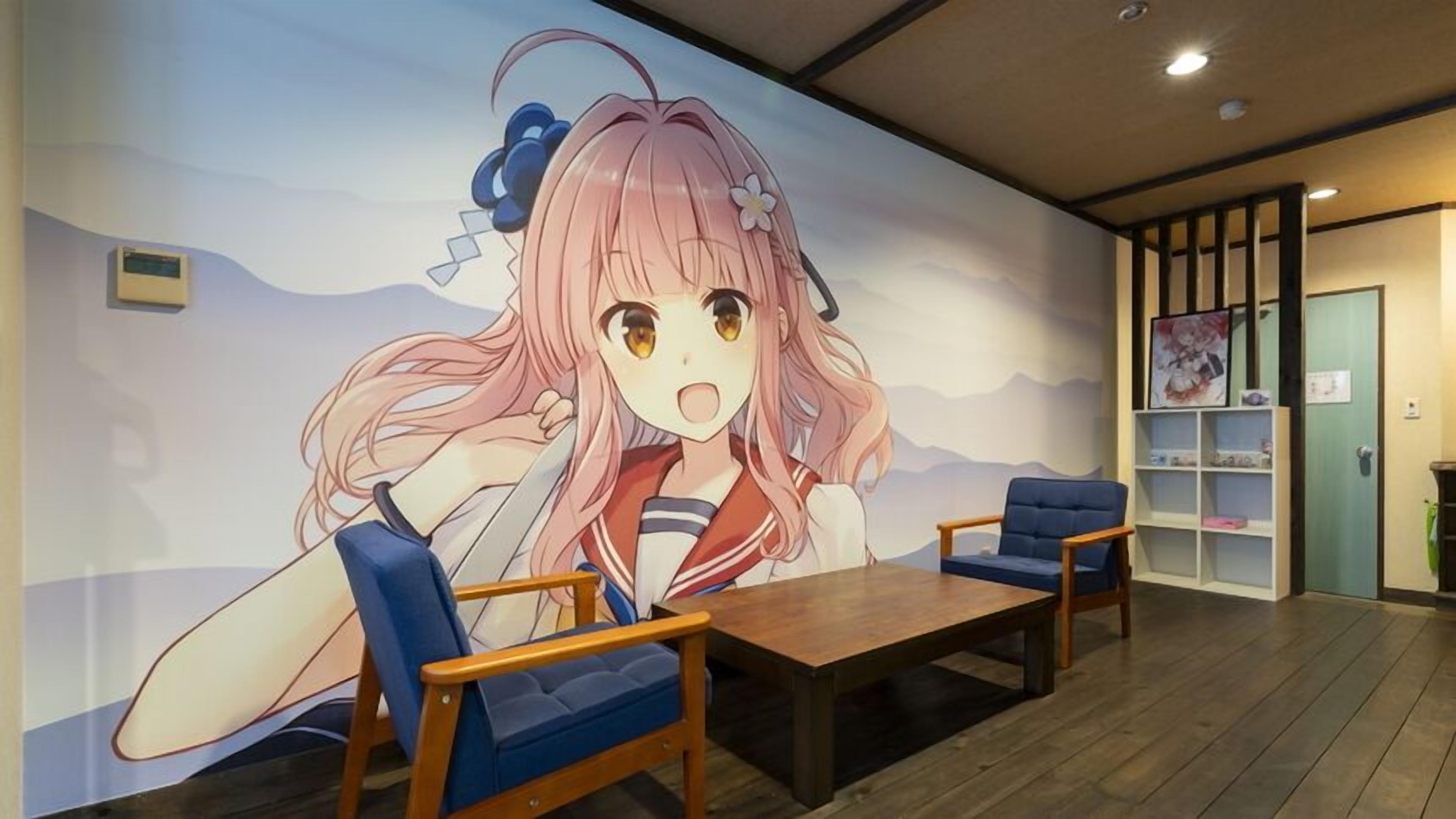 A room with a large anime mural, two blue chairs, a wooden table, and a bookshelf with anime posters.