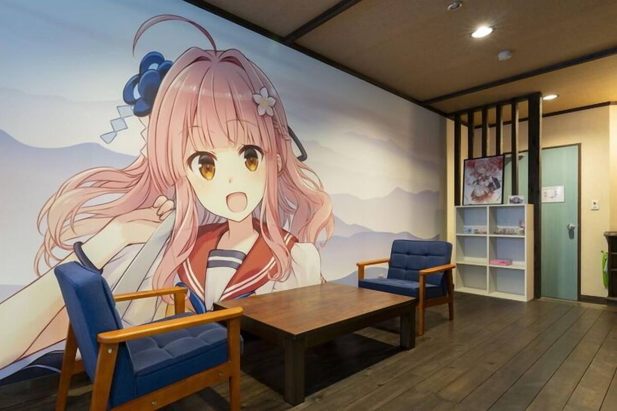 A room with a large anime mural, two blue chairs, a wooden table, and a bookshelf with anime posters.