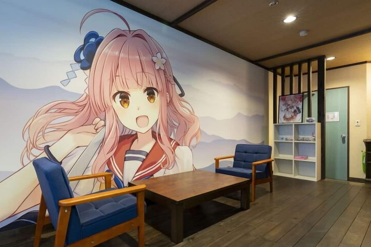 Una habitación con un gran mural de anime, dos sillas azules, una mesa de madera y una estantería con carteles de anime.