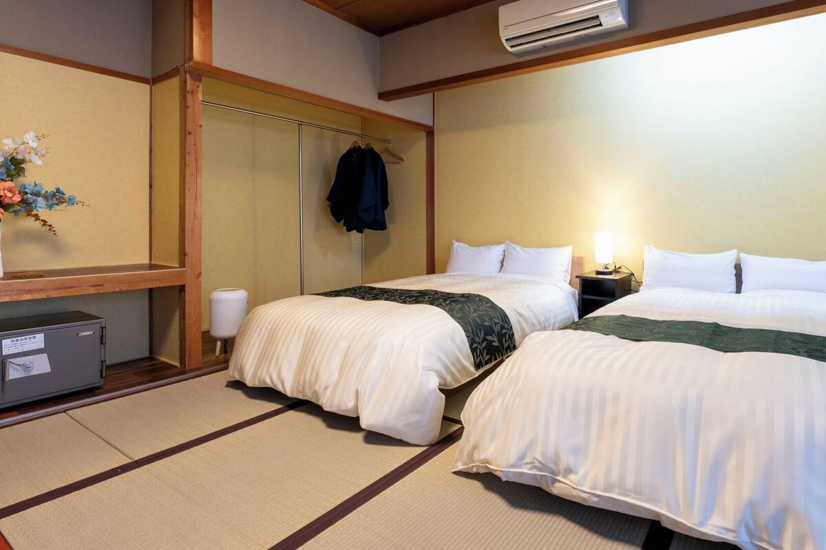A hotel room with two beds, a wardrobe, a bedside table with a lamp, and an air conditioning unit.