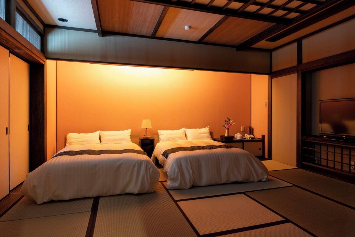 A traditional Japanese-style room with tatami flooring, two beds, a television, and a small table with a lamp and phone.