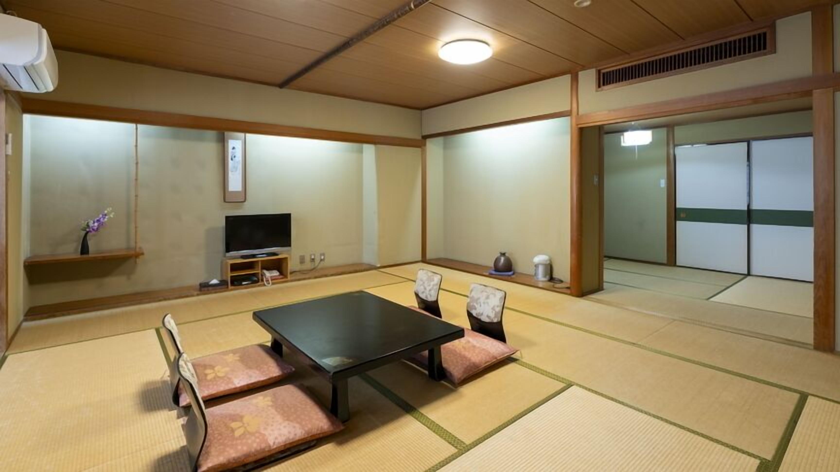 A tatami mat room with a black table, cushions, a television, and sliding doors.