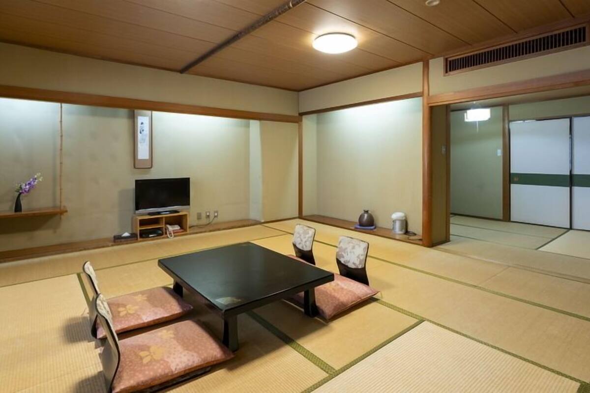 A tatami mat room with a black table, cushions, a television, and sliding doors.