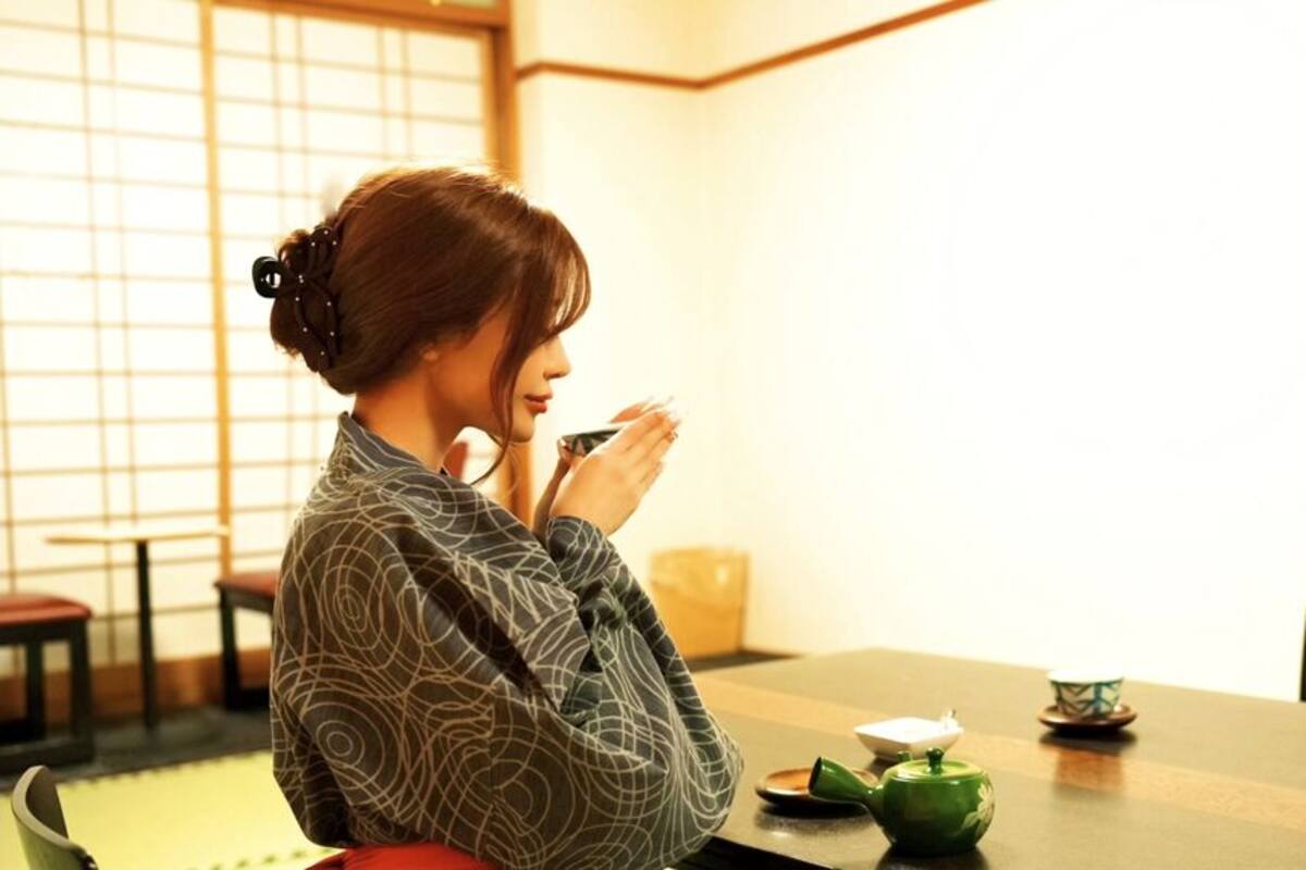 A person seated at a table with a teapot, cup, and saucer.